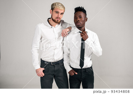 Joyful relaxed african and caucasian boys in white and black office clothes laughing and posing at white studio background with copy space 93434808