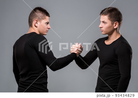 Portrait of young twin brothers standing face to face on gray ba 93434829