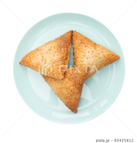 Three samsa sprinkled with sesame seeds are on a plate. White background. Isolated. Top view. 93435812