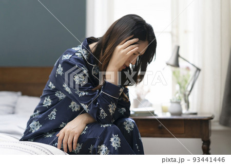 ベッドに座って頭を抱えるパジャマ姿のアラフィフの女性 93441446