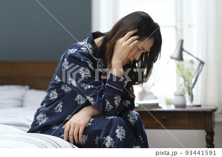ベッドに座って頭を抱えるパジャマ姿のミドル女性 93441591