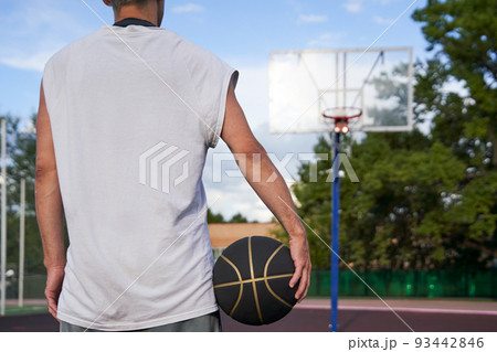 Man is standing with the ball in his hand on the background of the basketball court in the park. 93442846