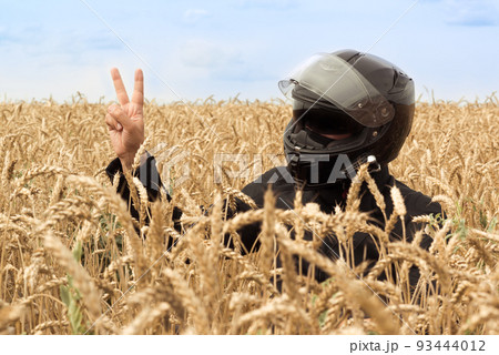 A male driver full motorcycle equipped. Outdoor wheat field and sky. Victory sign concept. Rider equipment 93444012