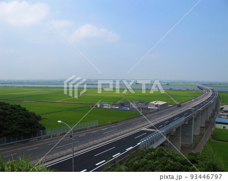 青空の下を走る高速道路と田んぼの爽やかな風景背景素材 93446797