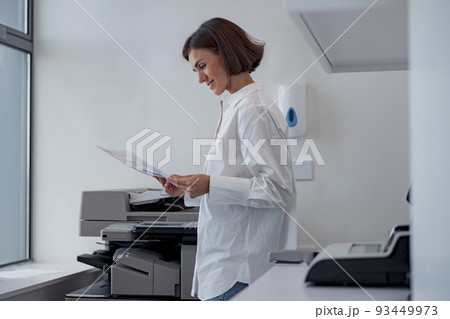 Smiling woman worker scanning a document on photocopy machine In modern office Smiling woman worker scanning a document on photocopy machine In modern office 93449973