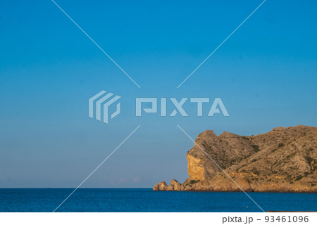 A large rocky promontory rises above the blue sea A large rocky promontory rises above the blue sea 93461096