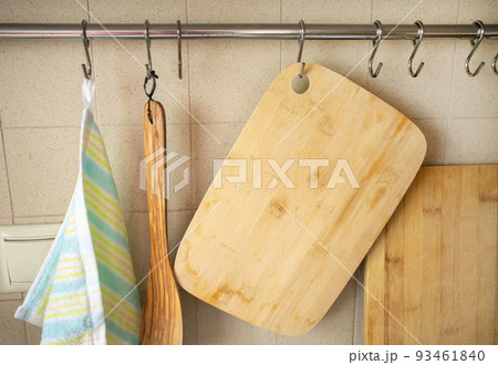 A close-up of cutting wooden boards, a cooking spatula, a kitchen towel hanging on hooks in the kitchen, against the background of a tiled wall 93461840
