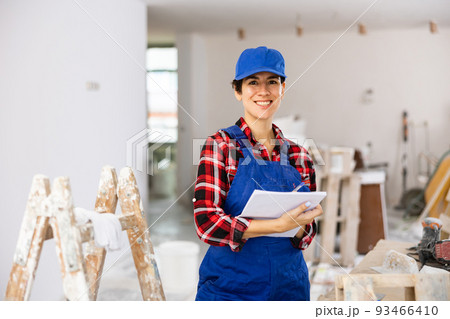 Woman in blue overalls checking completed construction work on drawing 93466410