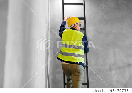 builder or worker in helmet climbing ladder 93470733