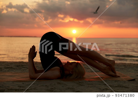 woman doing yoga plow pose on beach 93471380