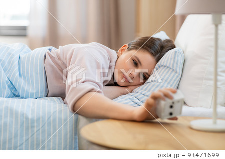 girl looking at alarm clock in bed in morning girl looking at alarm clock in bed in morning 93471699