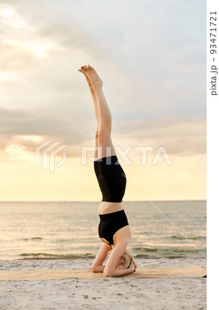 woman doing yoga headstand on beach 93471721