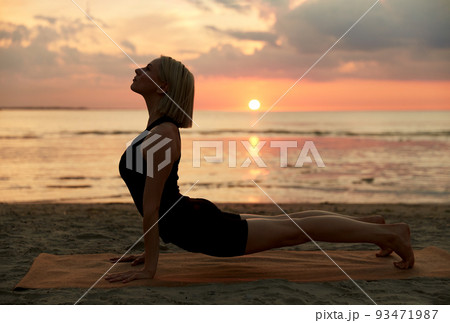 woman doing yoga upward facing dog pose on beach 93471987