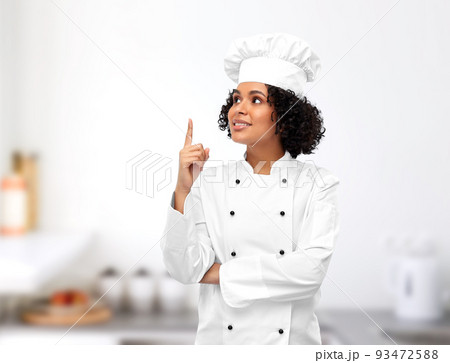 smiling female chef pointing finger up in kitchen smiling female chef pointing finger up in kitchen 93472588