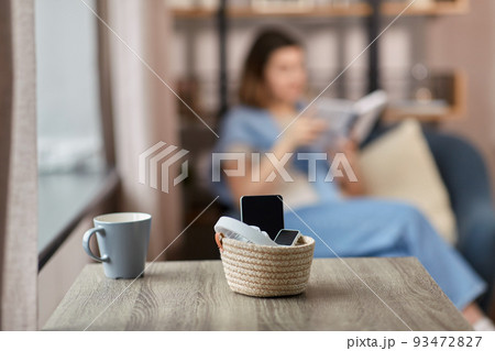 gadgets in basket on table and woman reading book 93472827