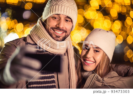 happy couple taking selfie over christmas lights happy couple taking selfie over christmas lights 93473303