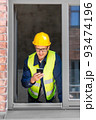 happy male builder with smartphone at open window 93474196