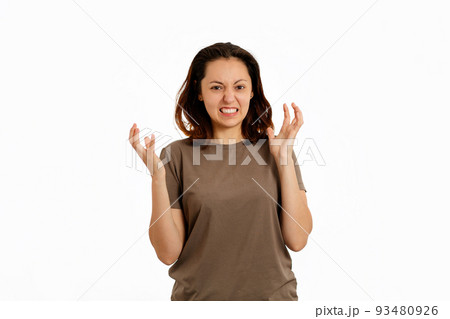 A young woman spread her hands in exasperation and clenched her teeth. White background. The concept of psychological problems and stress A young woman spread her hands in exasperation and clenched her teeth. White background. The concept of psychological problems and stress 93480926