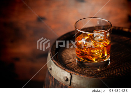 Glass of whiskey with ice cubes on the old barrel 93482428