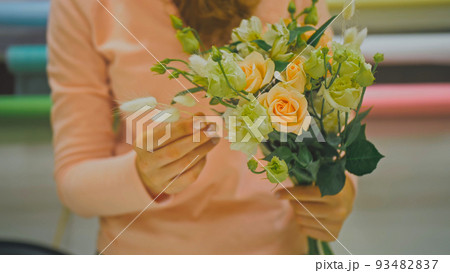 Female florist makes flower bunch, she cuts off wrapping paper w Female florist makes flower bunch, she cuts off wrapping paper w 93482837