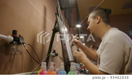 Man artist learns to paint with airbrush with acrylic dye, paper and easel. Concept modern art, airbrushing, aerography, graffiti, aerosol spray 93482838