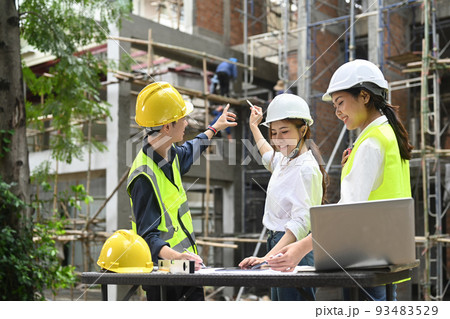 Architect team and real estate investor wearing safety helmets examining plans and discussing the construction process together Architect team and real estate investor wearing safety helmets examining plans and discussing the construction process together 93483529