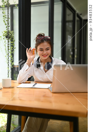 Cheerful young woman with wireless headphone chatting online, making video call via laptop computer 93483532