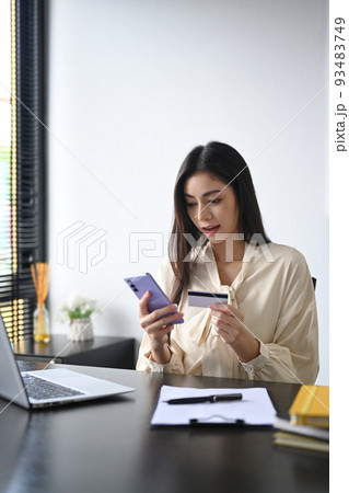 Beautiful young woman holding credit card, making payment on internet via smart phone. Online shopping, e-commerce concept 93483749
