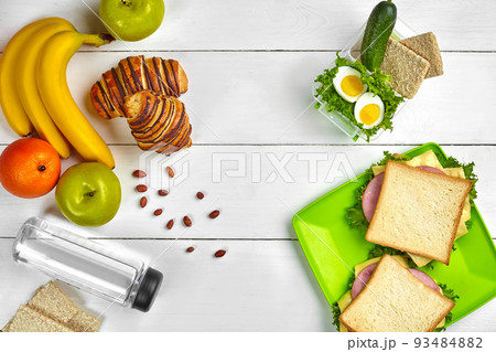 Lunch. Sandwich and fresh vegetables, bottle of water, nuts and fruits on white wooden background. Healthy eating concept. Top view with copy space 93484882