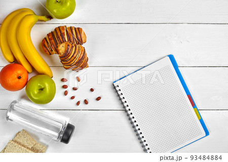 Planning concept. Fruits, croissants and notebook on white wooden background. Space for a text. Top view. 93484884