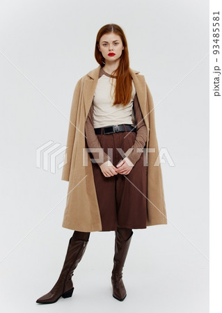 A red-haired model poses for a clothing catalog in a coat and boots on a white background. A banner for a clothing store. Full-length shot A red-haired model poses for a clothing catalog in a coat and boots on a white background. A banner for a clothing store. Full-length shot 93485581