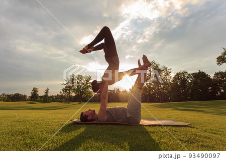 Healthy man lying on grass and balancing woman. Couple doing acrobatic yoga exercise in park Healthy man lying on grass and balancing woman. Couple doing acrobatic yoga exercise in park 93490097