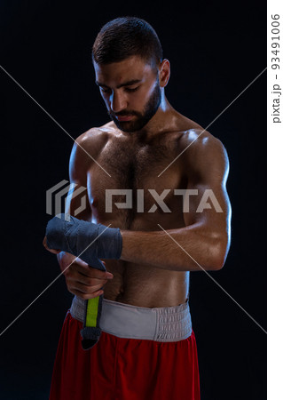 Sports boxer man pulls on the hand wrist wraps. Oriental male model isolated on black background. Sports boxer man pulls on the hand wrist wraps. Oriental male model isolated on black background. 93491006