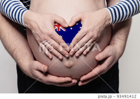 Australian family concept. Man embracing pregnant woman belly and heart with Australian flag Australian family concept. Man embracing pregnant woman belly and heart with Australian flag 93491412