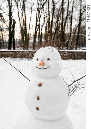 Sloppy tall snowman with carrot nose, walnut buttons stands alone in park field 93492421