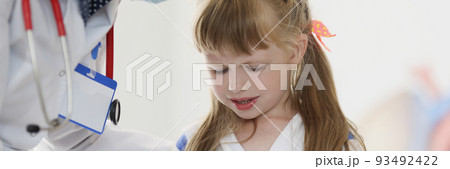 Doctor pediatrician in protective medical mask talking to little girl patient in clinic 93492422