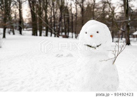 Sloppy tall snowman with carrot nose, walnut buttons stands alone in park field 93492423