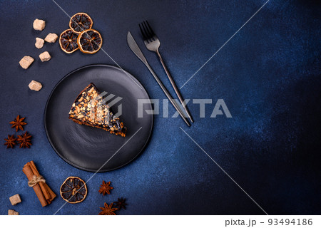 A piece of fresh delicious cake with nuts and chocolate on a black plate against a dark blue background A piece of fresh delicious cake with nuts and chocolate on a black plate against a dark blue background 93494186