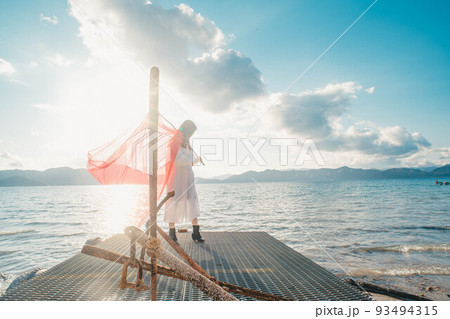 水辺で旗を掲げ楽しそうにする女性 93494315