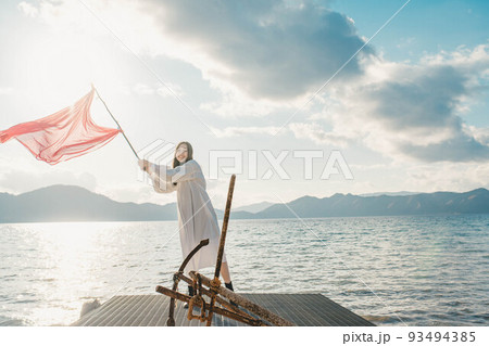 水辺で旗を振って楽しそうにしている女性 水辺で旗を振って楽しそうにしている女性 93494385