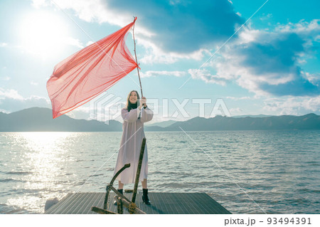 水辺で旗を振って楽しそうにしている女性 93494391