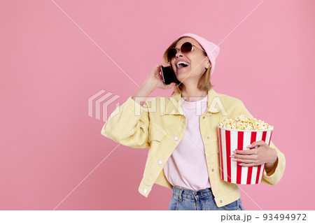 woman with bucket of popcorn talking on the phone woman with bucket of popcorn talking on the phone 93494972
