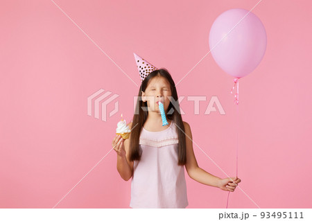 happy little birthday girl with party cone holding cupcake 93495111
