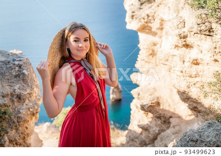 A woman in a red flying dress fluttering in the wind, against the backdrop of the sea. 93499623