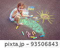 Child from Ukraine draws with chalk. 93506843