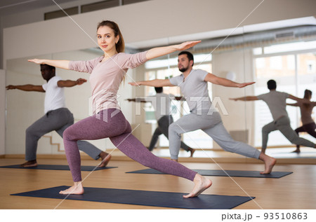 Woman and men practising warrior II pose 93510863