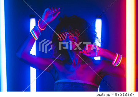 Fashionable woman with afro hairstyle dancing in room with colorful lamps. Cyberpunk style or Fashionable woman with afro hairstyle dancing in room with colorful lamps. Cyberpunk style or 93513337