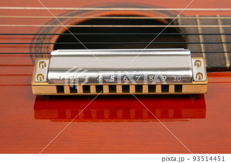 The harmonica rests on the body of a classical guitar. Classical musical wind instrument. 93514451