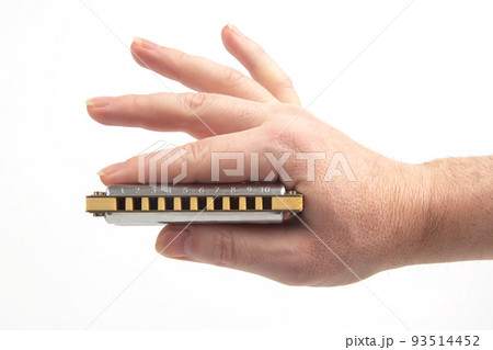 The right hand holds a harmonica on a white background. Classical musical wind instrument. 93514452