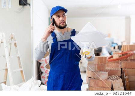 Builder with documents is talking on a mobile phone 93521044